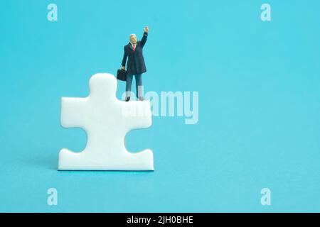 Miniature people toy figure photography. A businessman standing above puzzle jigsaw piece while raise his hand. Isolated on blue background. Image pho Stock Photo