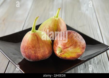 Fresh figs in black plate on wooden background. Stock Photo