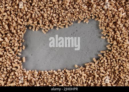 From above of heap of solid wood biofuel pellets scattered on gray table with rectangular shaped hole Stock Photo