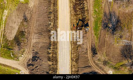 Above top view on base of new road under construction, foundation, excavator is digging soil, arranging the terrain along the road, the workers put in Stock Photo