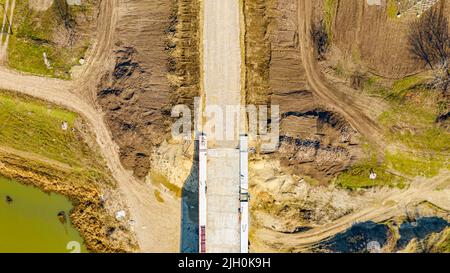 Above top view on gravel, fraction, base of new road under construction and beginning of bridge under construction at building site. Stock Photo