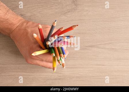 Hand of a man holding a group of colored pencils on a wooden table. Top view Stock Photo