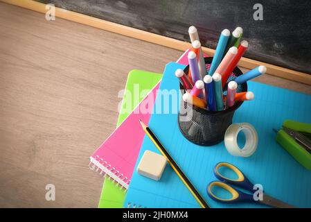 School supplies with pen with markers on notebooks with tools on wooden desk and blackboard. Elevated view. Horizontal composition. Stock Photo