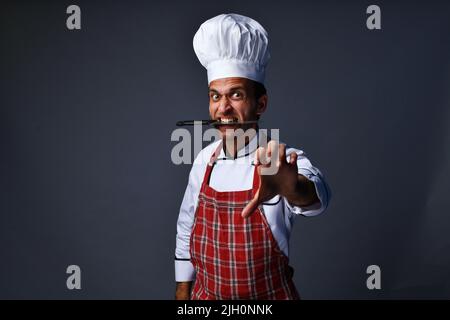 Male chef posing angry expression with knife in mouth Stock Photo