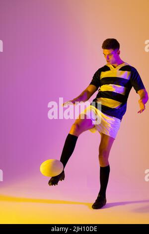 Caucasian male rugby player kicking rugby ball over pink lighting Stock Photo