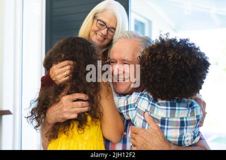 Multiracial grandchildren embracing cheerful grandparents and welcoming them at home at entrance Stock Photo