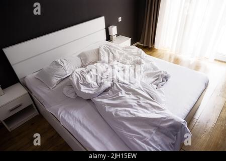 Crumpled white bed with set of white bed linen in bedroom in the early morning Stock Photo