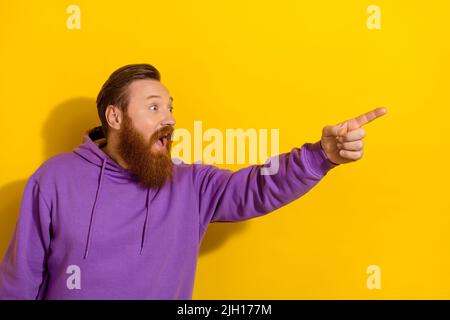 Photo of funny impressed guy dressed purple sweater looking pointing finger empty space isolated yellow color background Stock Photo