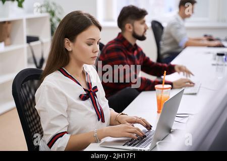 People working in modern IT office. Group of young and experienced programmers and software developers sitting at desks working on computers. Team at Stock Photo