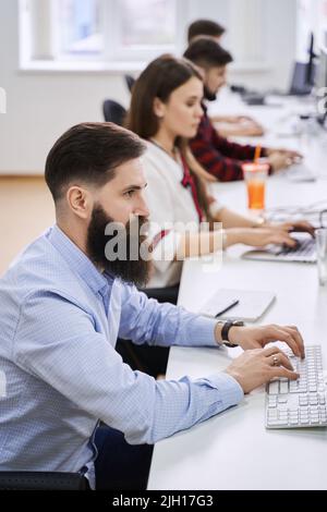 People working in modern IT office. Group of young and experienced programmers and software developers sitting at desks working on computers. Team at Stock Photo