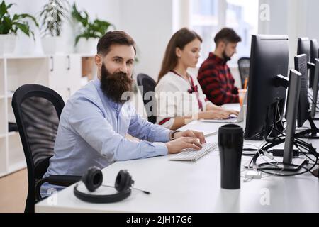 People working in modern IT office. Group of young and experienced programmers and software developers sitting at desks working on computers. Team at Stock Photo