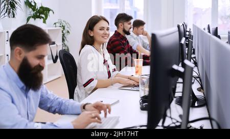 Junior female professional working in modern IT office. Group of young and experienced programmers and software developers sitting at desks working on Stock Photo
