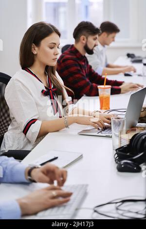 People working in modern IT office. Group of young and experienced programmers and software developers sitting at desks working on computers. Team at Stock Photo