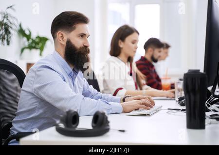 People working in modern IT office. Group of young and experienced programmers and software developers sitting at desks working on computers. Team at Stock Photo
