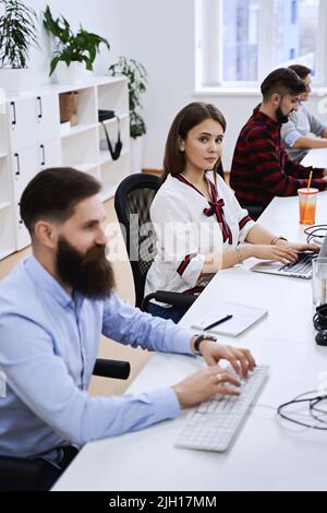 People working in modern IT office. Group of young and experienced programmers and software developers sitting at desks working on computers. Team at Stock Photo