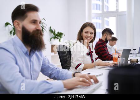 People communicating and working in modern IT office. Group of young and experienced programmers and software developers sitting at desks working on Stock Photo