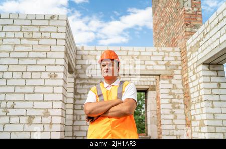 Successful builder in hardhat controls quality of work at construction site. Inspection and engineering in new house building. Stock Photo