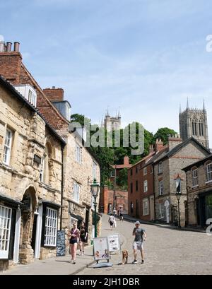 Lincoln, Lincolnshire, UK, June 16  2022 Pedestrians walk down the cobbled Steep Hill, a road worthy of it's name. The cathedral is in the background. Stock Photo