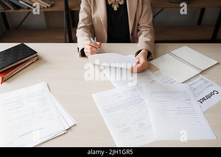 Unrecognizable woman reading document at her office desk, free space. Business woman working on paperwork, top view. Stock Photo