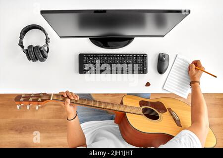 man with guitar writing to music book at table Stock Photo