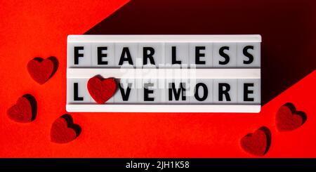 Lightbox with text FEAR LESS LOVE MORE. Motivational Words Quotes Concept with red hearts. Colorful red background. Minimalistic creative concept. Stock Photo