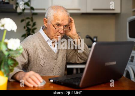 desperate old man pensioner chatting online via laptop with friends at home Stock Photo