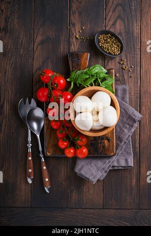 Caprese salad, ingredients for cooking. Cutting wooden board with traditional caprese preparation ingridients: mozzarella, tomatoes , basil, olive oil Stock Photo