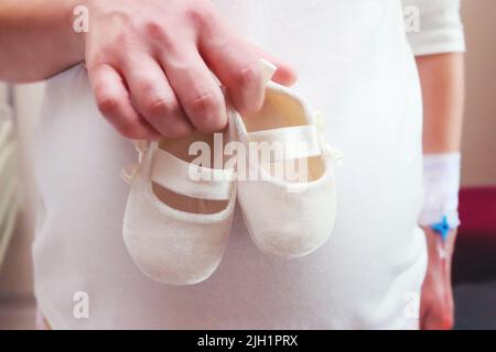 Newborn baby booties in mother's hands. Pregnant woman belly, Happy parents concept Stock Photo