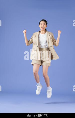 Energetic young asian woman jumping isolated on purple studio background. Excited female celebrating win Stock Photo