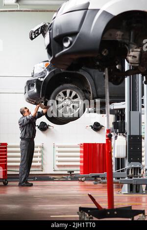 Mechanic removing engine protection on raised car Stock Photo