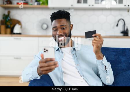 Online transaction, payment. Multiracial man holding credit card and using smartphone for shopping, a dark skinned guy with mobile phone and making purchases online Stock Photo