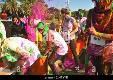 Teenage girls, some wearing Hijabs, joyfully grab and throw colored powder at each other at the Color Walk in Dubai, United Arab Emirates. Stock Photo