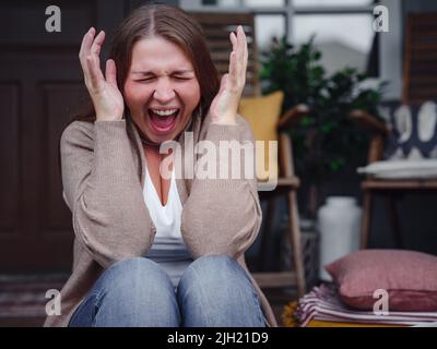 middle aged depressed woman sitting on porch. She feeling sad and worried suffering depression in mental health. Problems and broken heart concept. Negative human emotion with cry of pain Stock Photo