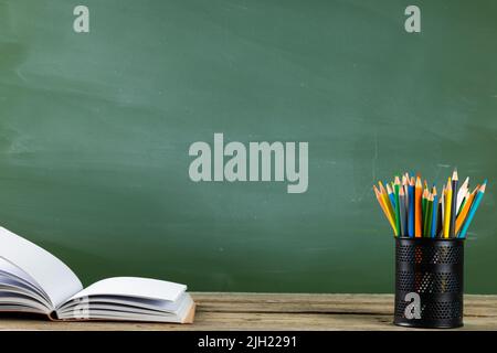 Image of books, notebook and crayons on wooden table over black board Stock Photo