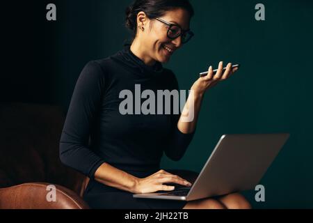 Smiling woman speaking on cellphone and working on laptop computer in office. Beautiful asian female using laptop and talking on mobile phone in offic Stock Photo