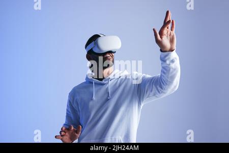 Happy young man touching virtual space with his hand. Cheerful young man experiencing a fun 3D simulation. Young man interacting with the metaverse us Stock Photo