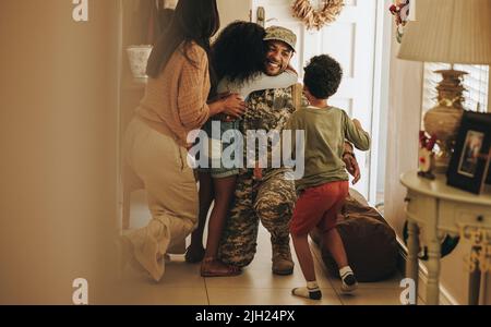 Heartwarming military homecoming. Happy soldier reuniting with his wife and children after serving in the army. Cheerful serviceman embracing his fami Stock Photo