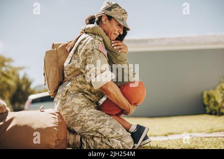 Military mom embracing her son after returning home from the army. Courageous female soldier having an emotional reunion with her young child after mi Stock Photo