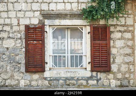 Closed window with opened brown shutters of an old coastal house Stock Photo