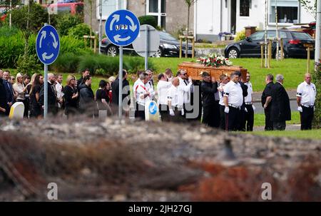 The coffin of John Steele is carried by mourners up Churchill Road, past the remnants of the bonfire from which he fell, following his funeral service at his house in Larne, County Antrim. Mr. Steele fell to his death on Saturday while helping to build a bonfire. Picture date: Thursday July 14, 2022. Stock Photo