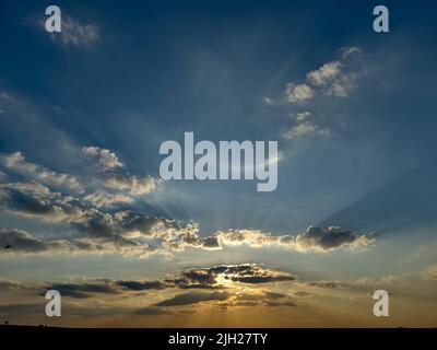Dramatic sunset with rays and the sun behind the clouds. Stock Photo