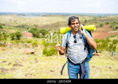 Excited happy middle aged man talking on mobile phone call during trekking on top of hill - concept of connection, technology and communication. Stock Photo