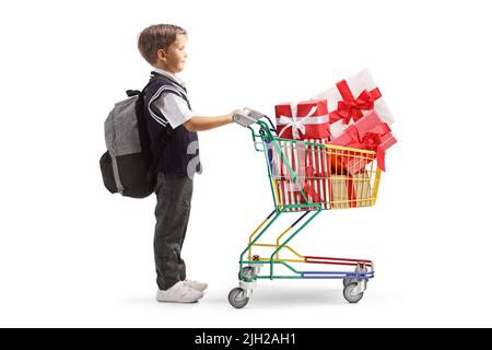 Full length profile shot of a schoolboy in a uniform with a small shopping cart full of presents isolated on white background Stock Photo