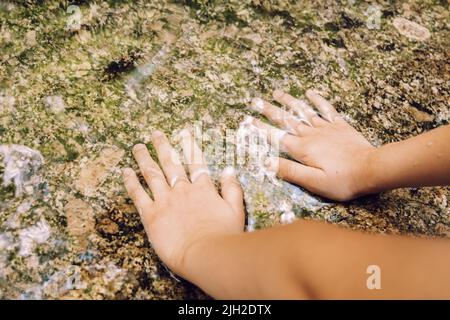 Kid touches cold water in waterfall Stock Photo