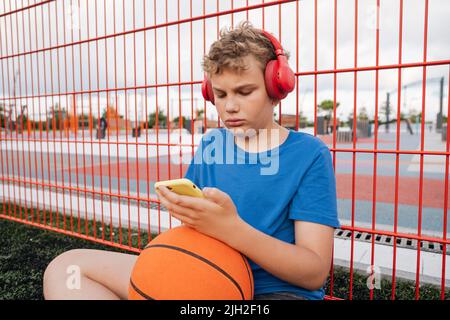 Portrait of a boy with a basketball and headphones on the playground. Stock Photo