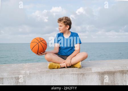 Portrait of a boy with a basketball on the sea and sky. Stock Photo