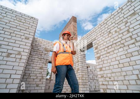 Foreman in helmet and uniform with walkie-talkie in hand at construction site. Construction and development concept. Stock Photo