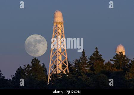 View of a moon rise from Mt Wilson Observatory in Los Angeles County shown against the 150-ft Solar Telescope amid pine trees. Stock Photo