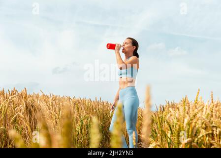 Sporty woman in the countryside drinking water from a glass bottle. Stock Photo