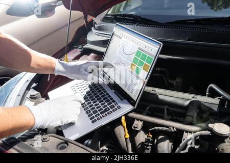 Young Male Mechanic Using Laptop While Examining Car Engine Stock Photo